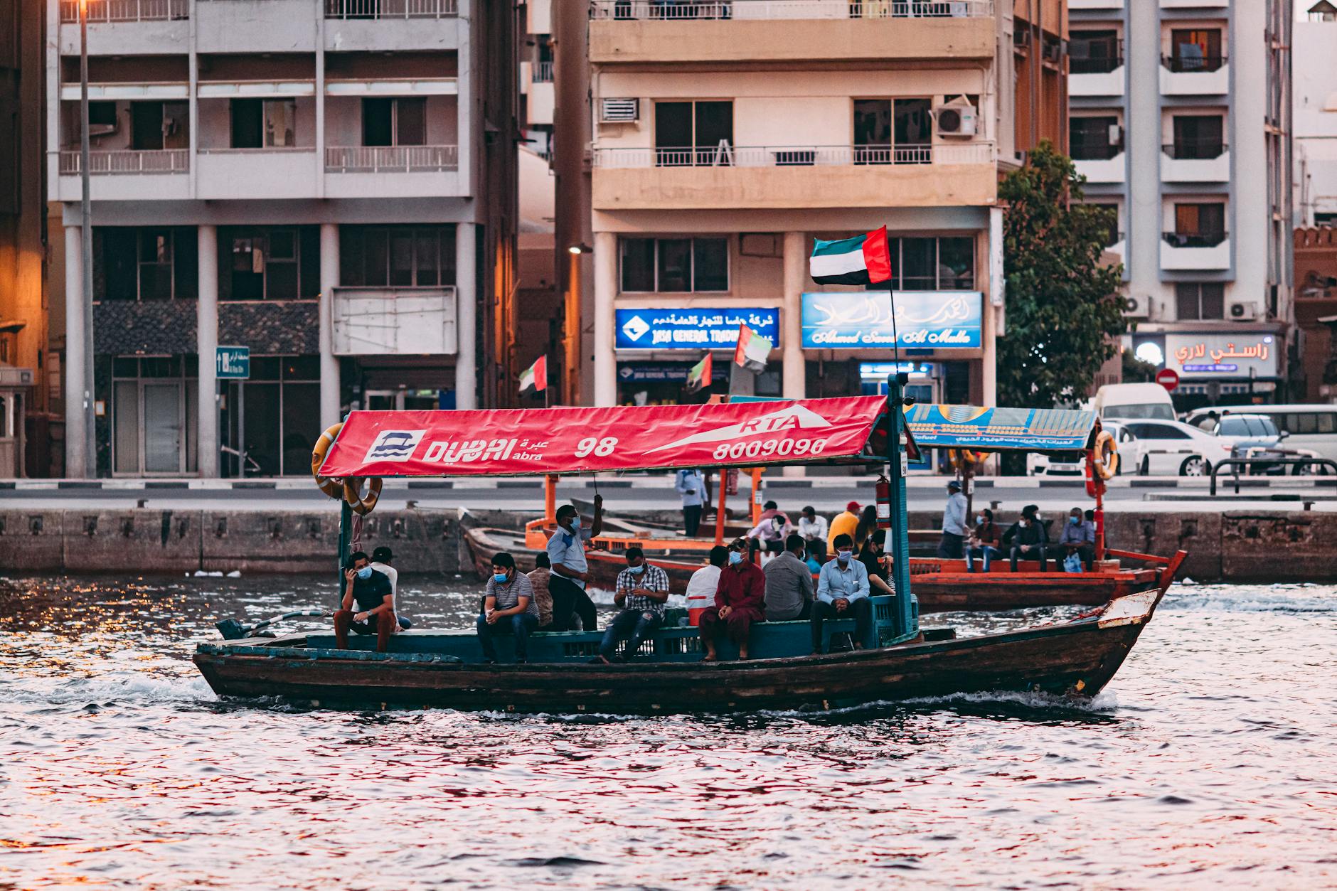 Pasażerowie na łodzi abra płynącej po Dubai Creek o zachodzie słońca
