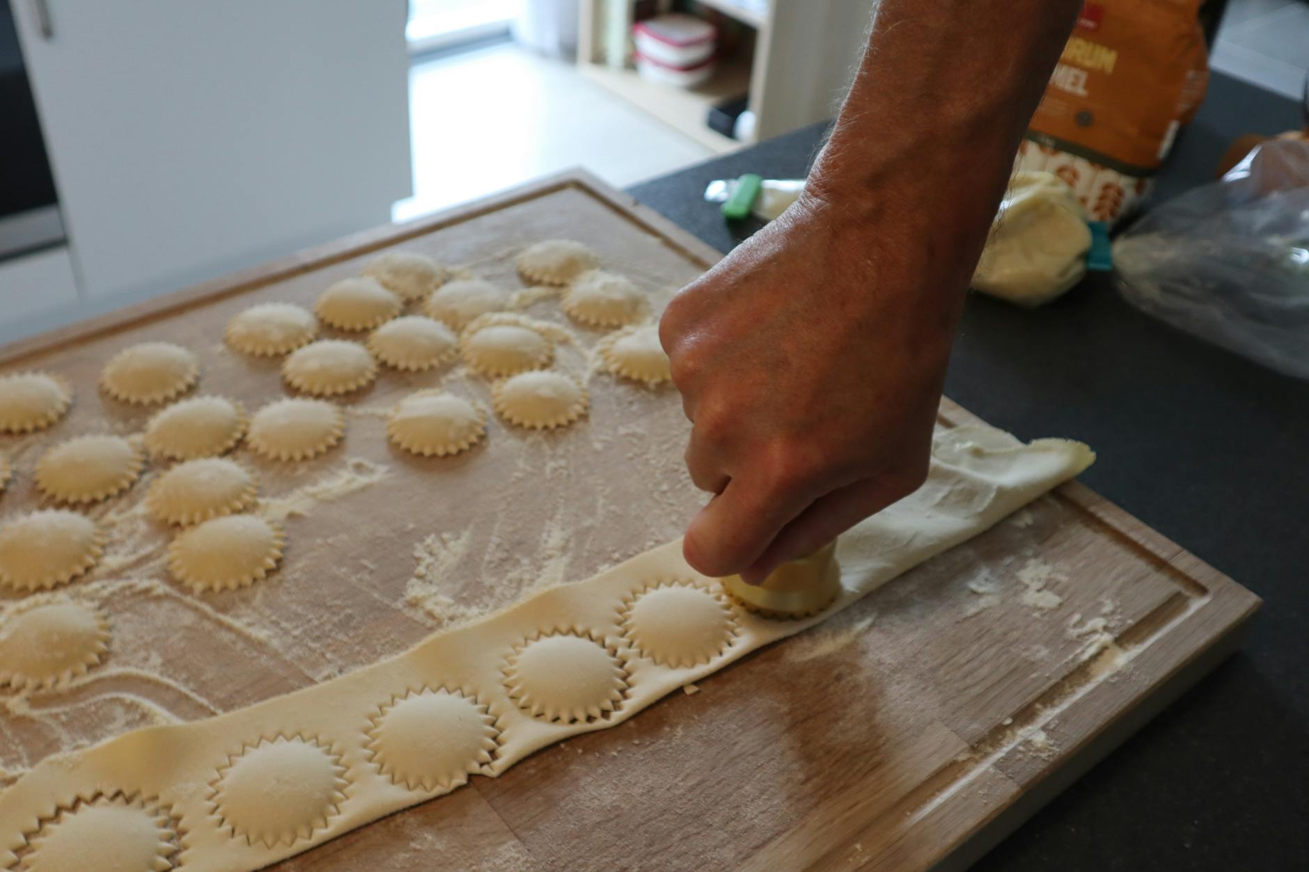 Ręce lepią domowe ravioli na oprószonej mąką stolnicy w kuchni