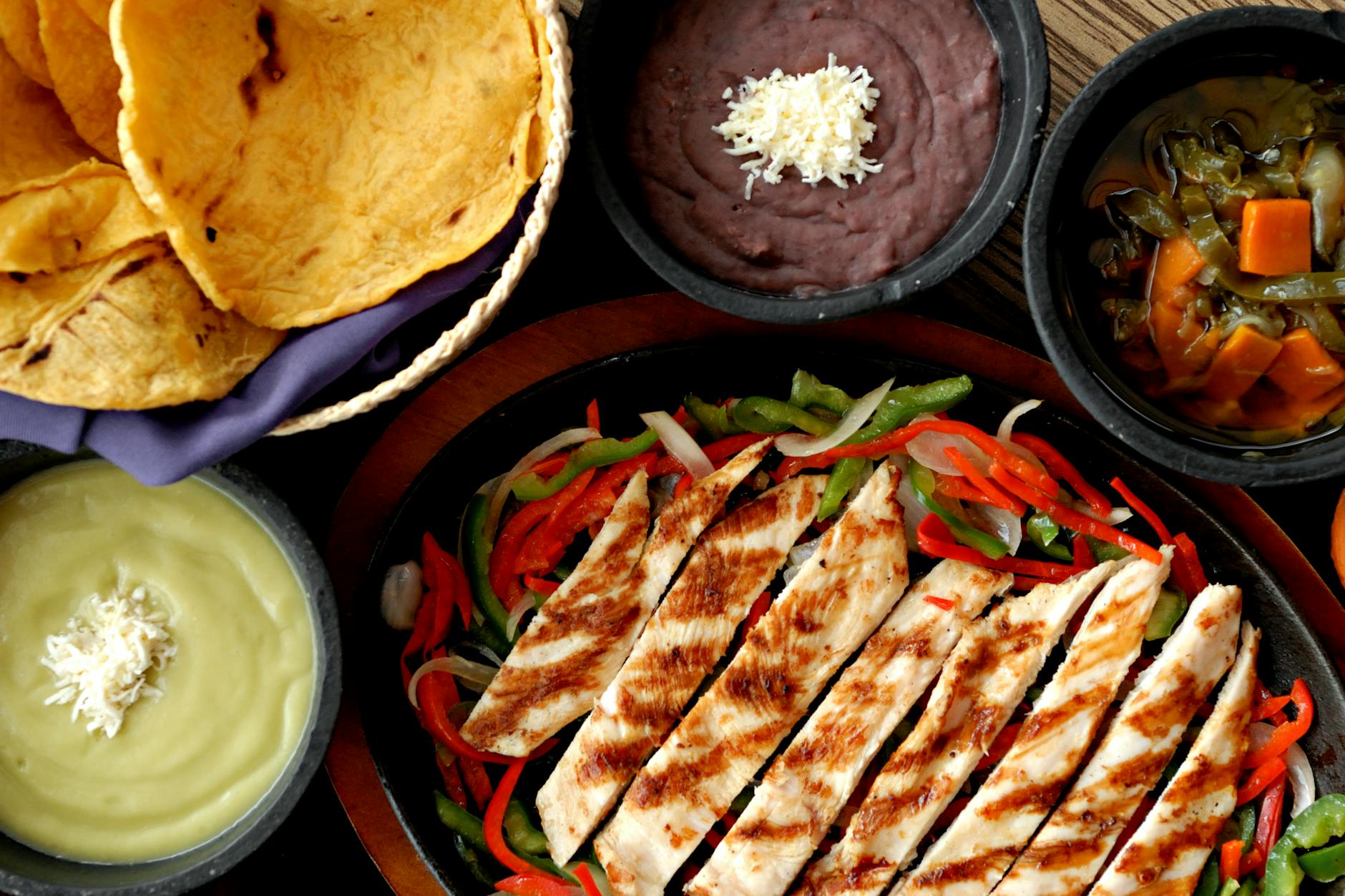 Talerz z grillowanymi fajitas z kurczaka, tortillami, fasolą i salsami