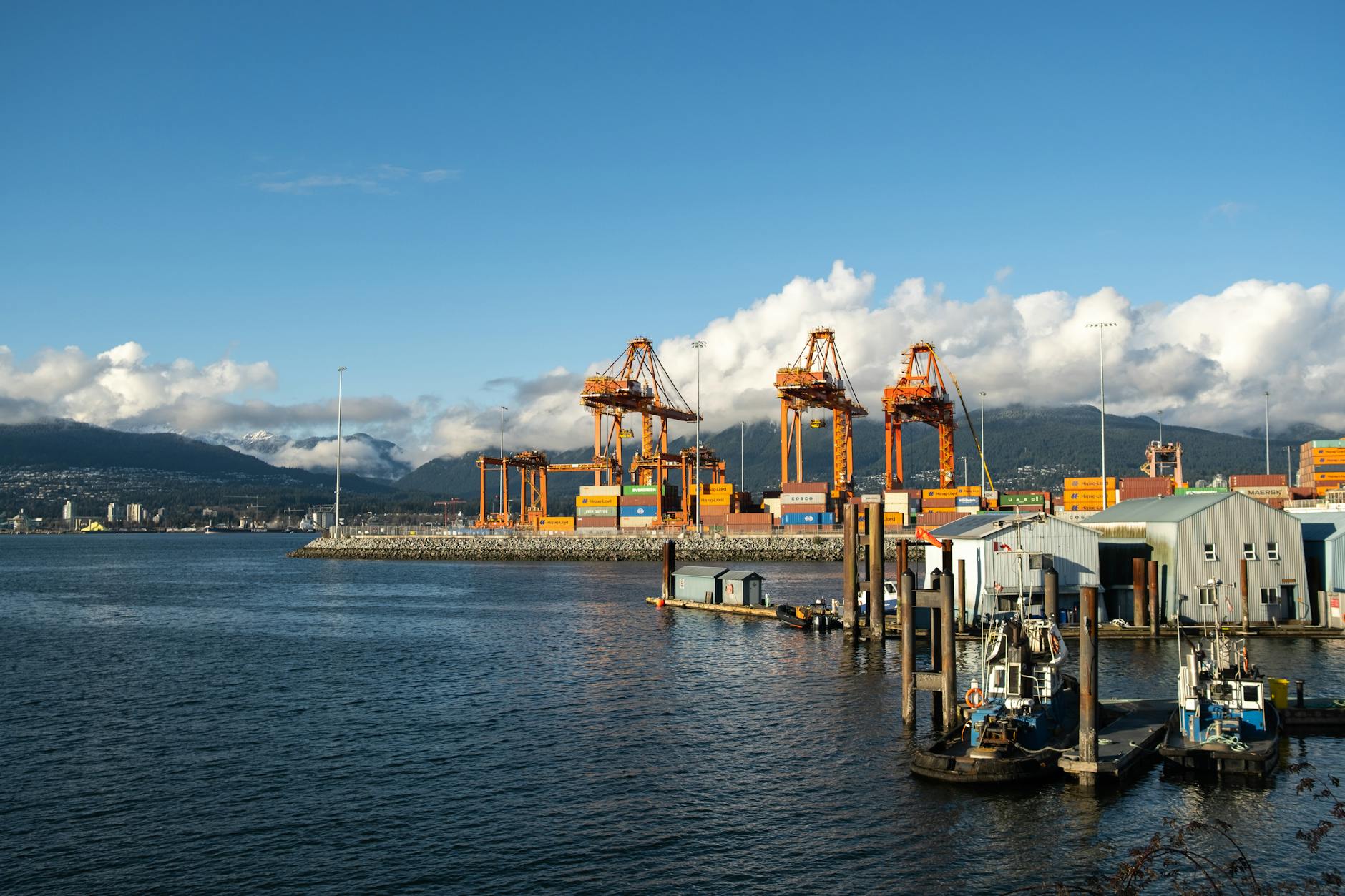 Kanadyjski port kontenerowy z pomarańczowymi dźwigami i górami w tle Kanadyjski port kontenerowy z pomarańczowymi dźwigami i górami w tle