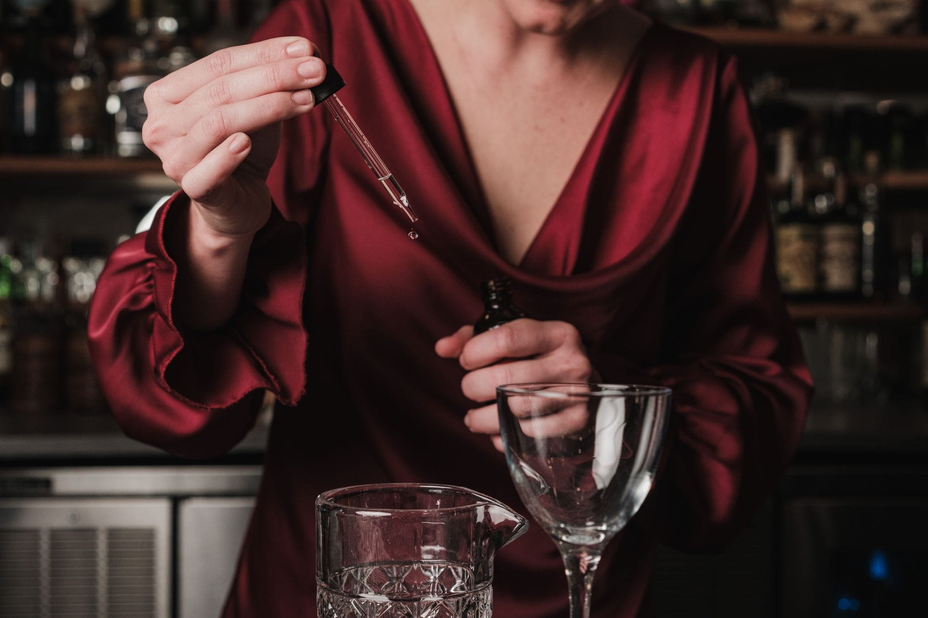 Barmanka w czerwonej sukience dodaje domowy bitter do koktajlu w barze